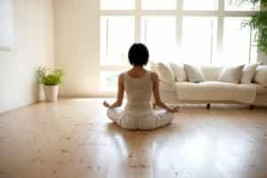 Yamanashi Prefecture, Japan. low-angle view of woman in yoga pose on wooden living room floor with large windows letting in lots of natural sunlight